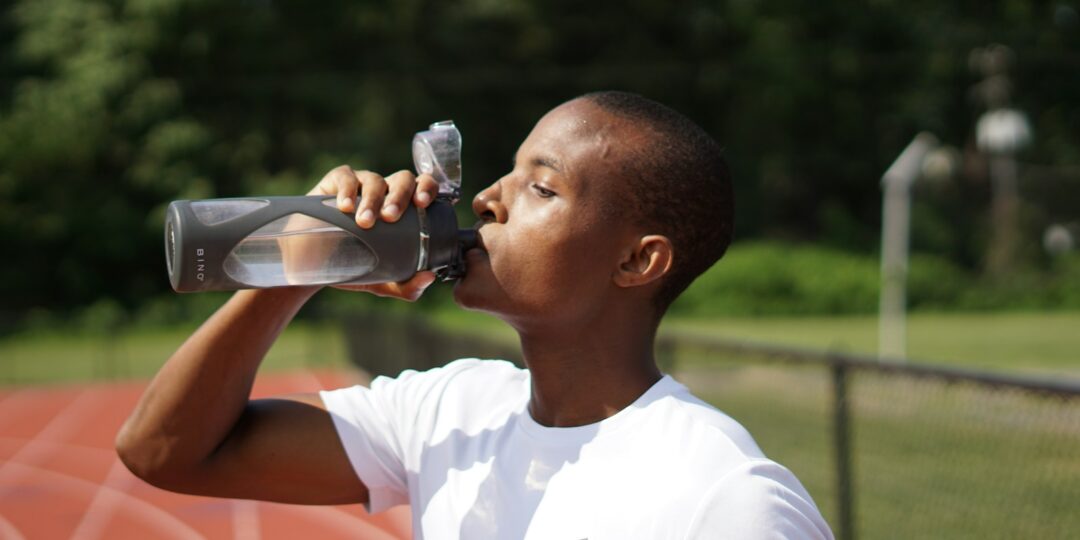 man in white crew neck t-shirt drinking from black sports bottle