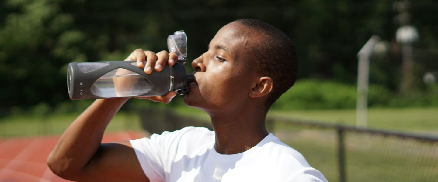 man in white crew neck t-shirt drinking from black sports bottle